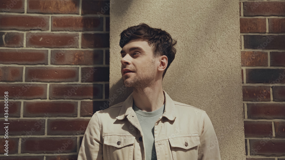 smiling man in beige jacket looking away near building outside. smiling man in beige jacket looking away near building outside.