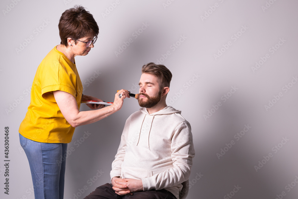 Obraz premium Bearded man getting makeup. Woman visagist works with brush. Copyspace