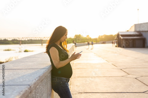 Pregnant woman with smartphone outdoors. Pregnancy, technology and communication concept