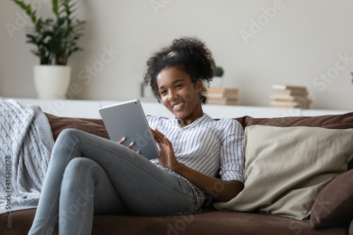 Happy relaxed young african american multiracial woman enjoying watching funny photo or video content, using digital computer tablet, shopping in internet store, playing games or web surfing online.