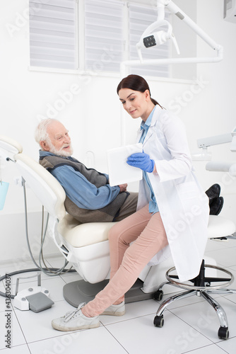 senior patient lying in dental chair and taking consultation from doctor with tablet in hands.