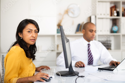 Canvas Print Portrait of busy latin american female office employee working at desk with computer
