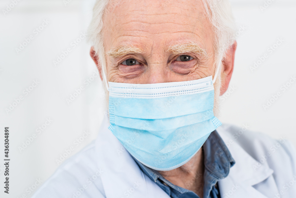 portrait of senior doctor in white coat and medical mask on grey background. portrait of senior doctor in white coat and medical mask on grey background.