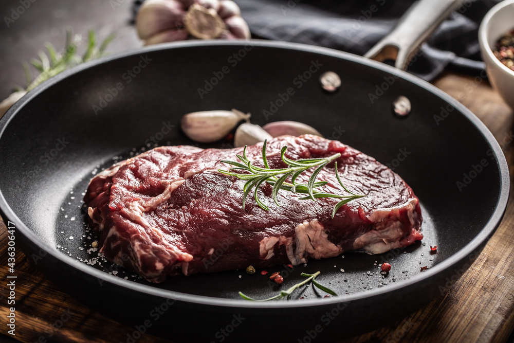 Fresh raw beef Ribe Eye steak in teflon pan with rosemary, garlic, salt and pepper