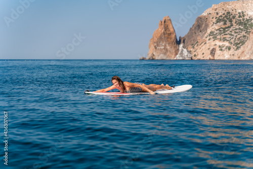 Sporty girl on a glanders surfboard in the sea on a sunny summer day. In a striped swimsuit, lying on his stomach, rowing with his hands. Summer activities by Stortom by the sea. © svetograph