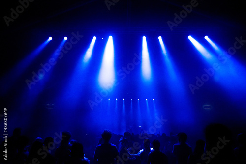 Crowd of people partying at live concert, blue stage lights