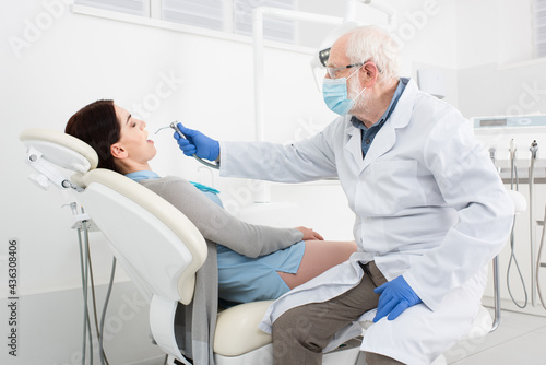 senior dentist in medical mask making teeth treatment of patient in dental chair.