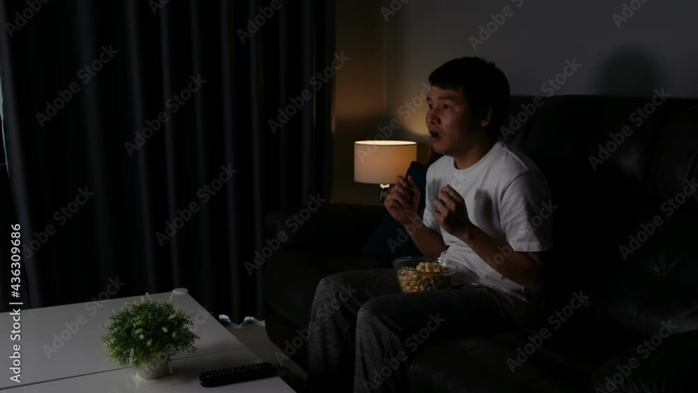Scared young man is watching horror movie TV on sofa at night Scared young man is watching horror movie TV on sofa at night