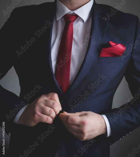 Man in a blue suit and red tie buttoning his suit jacket