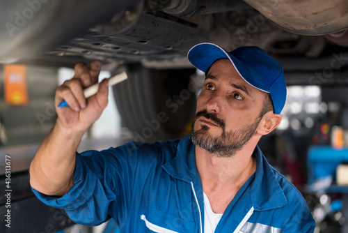 Auto mechanic in work clothes inspects a car in a workshop of a car. A car mechanic holding pen.