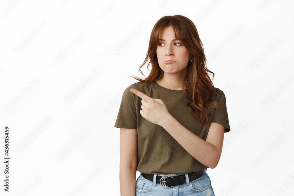 Upset girl show unfair thing, pointing and looking left with sulking sad face, complaining, staring with jealous disappointed expression, standing against white background Upset girl show unfair thing, pointing and looking left with sulking sad face, complaining, staring with jealous disappointed expression, standing against white background