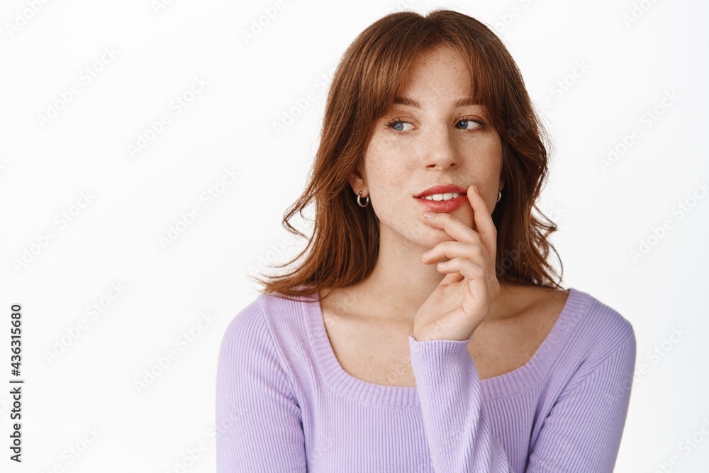 Stylish young woman with make up, red lips, looking aside thoughtful, smiling and pondering, standing against white background in purple blouse Stylish young woman with make up, red lips, looking aside thoughtful, smiling and pondering, standing against white background in purple blouse