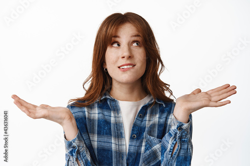 I dont know. Confused redhead girl shrugging and looking up with indecisive, unsure face, cant make decision, have no clue, standing puzzled against white background