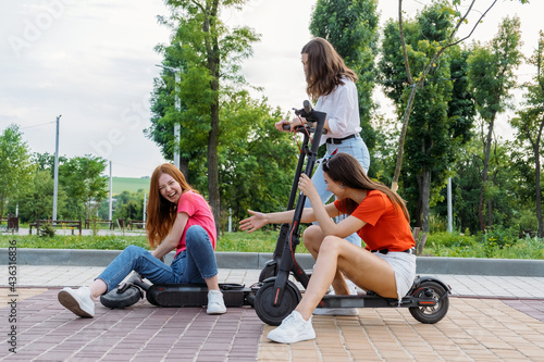 Three Young girl friends on vacation having fun driving electric scooter through the city park. Ecological and urban city transport, summer leisure activities concept © irissca