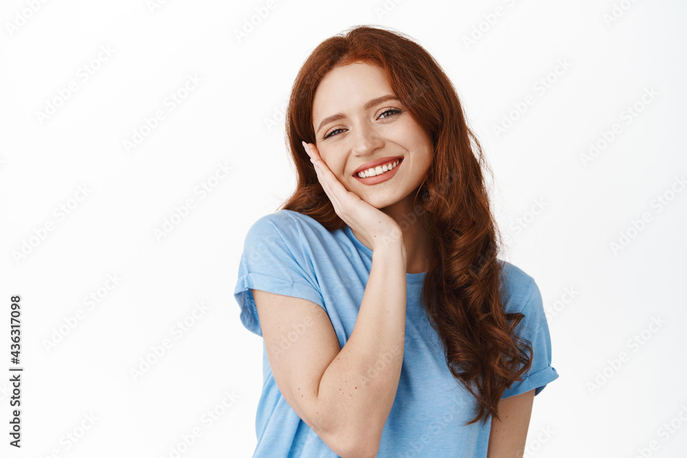 Adorable young woman with fresh and clean natural skin, red hair, touching cheek and smiling happy and satisfied, using cleansing facial skincare cosmetic, standing over white background Adorable young woman with fresh and clean natural skin, red hair, touching cheek and smiling happy and satisfied, using cleansing facial skincare cosmetic, standing over white background