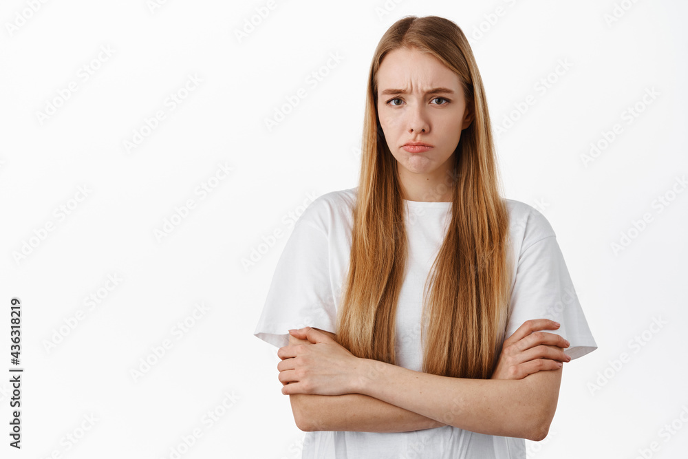 Image of angry offended blond girl, sulking and frowning upset about unfair thing, cross arms on chest and pouting disappointed, standing over white background Image of angry offended blond girl, sulking and frowning upset about unfair thing, cross arms on chest and pouting disappointed, standing over white background
