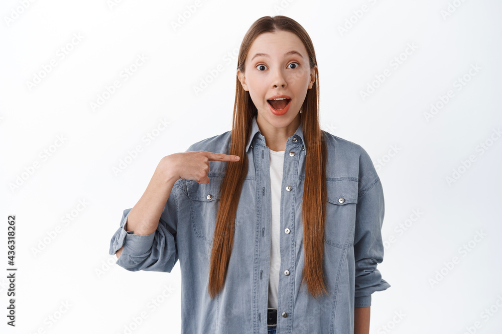 Is it me. Surprised cheerful girl points at herself with fascinated happy face, being chosen, winning, standing over white background Is it me. Surprised cheerful girl points at herself with fascinated happy face, being chosen, winning, standing over white background