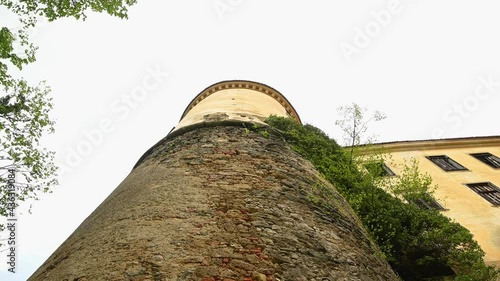 Handheld establishment shot of abandoned castle in Slovenia. Low angle view of ancient round tower with broken windows. Middle age ruins. Climbing plant leaves sway in breeze. Real time, wide angle photo