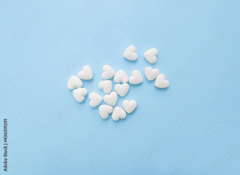 White pills in the shape of hearts on a pastel blue background White pills in the shape of hearts on a pastel blue background