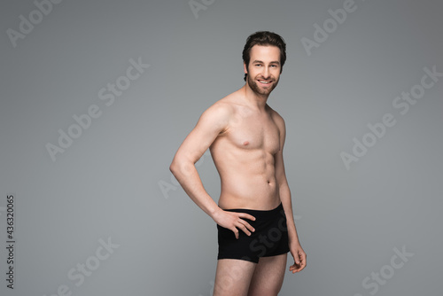 happy shirtless man in black underwear posing with hand on hip isolated on grey.