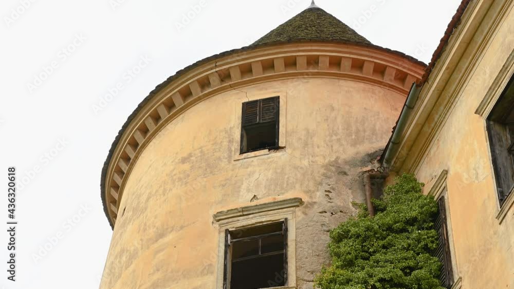 Handheld establishment shot of abandoned castle in Slovenia. Ancient tower with broken windows. Walls overgrown with climbing plants. Middle age ruins