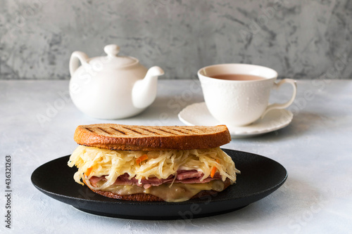 Reuben sandwich is a classic American hot sandwich with sliced beef, Swiss cheese, sauerkraut and sauce. Teapot and a cup of tea on the table. photo