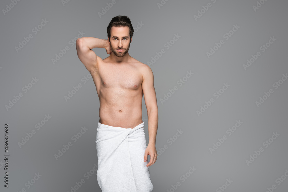 Fototapeta premium muscular man wrapped in white towel posing isolated on grey.
