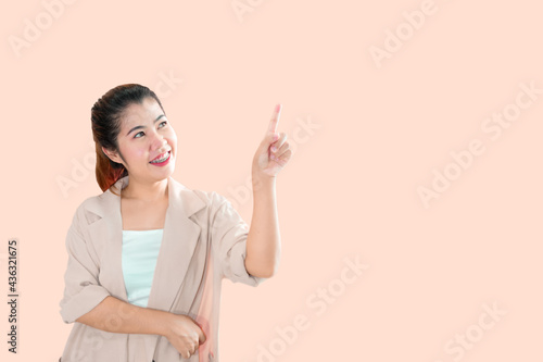 A young Asian woman standing, pointing the index finger of her left hand upward with a smiling face.