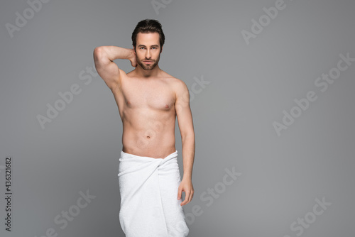 muscular man wrapped in white towel posing isolated on grey.