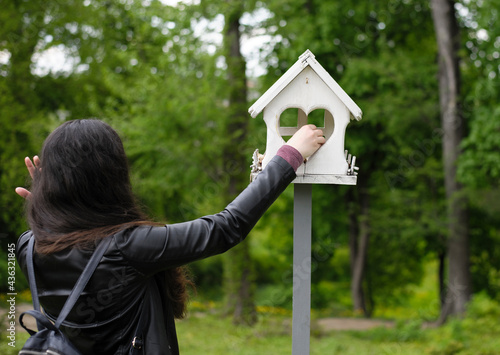 girl feeds birds in a feeder in an spring park, back view. girl puts food. taking care of birds, natural green background, bokeh, focus. wooden birdhouse. white bird feeder and woman in the garden © Oleksandr Filatov