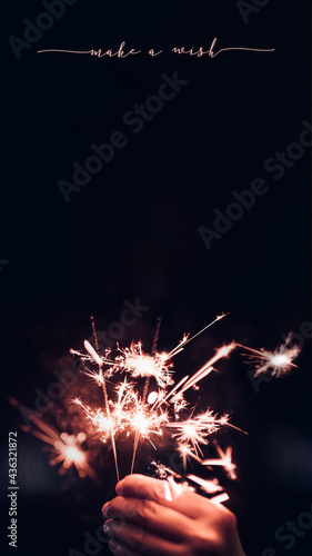 Fotografia Make a wish new year 2022 with hand holding burning Sparkler firework blast with on a black bokeh background at night,holiday celebration event party