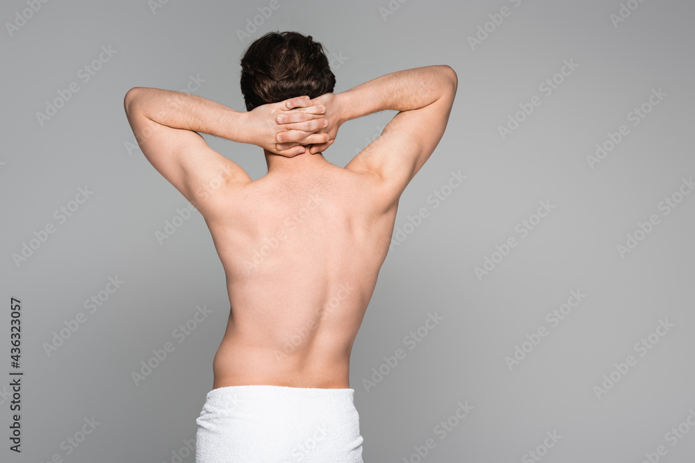back view of shirtless man wrapped in towel standing with hands on neck isolated on grey.