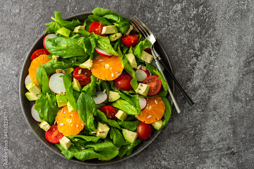 Delicious healthy salad of spinach leaves, tangerine and avocado slices, tomato and radish with seeds, salad in a plate close-up with forks, top view, copy space