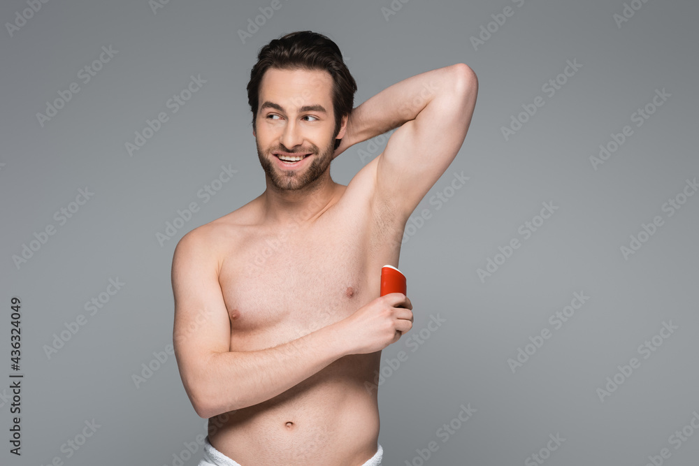 Fototapeta premium cheerful shirtless man applying solid stick deodorant isolated on grey.