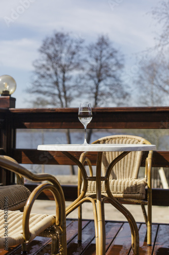A glass of white wine on a white table on the terrace. Glare from a glass of wine and sunbeams