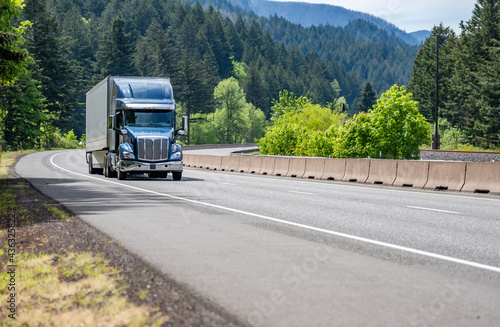 Shiny blue big rig semi truck transporting cargo in dry van semi trailer running on the winding road in Columbia Gorge