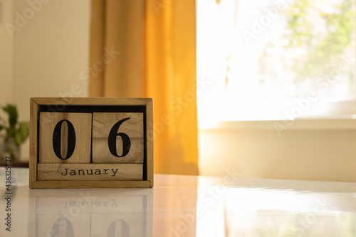 Valokuva Wooden blocks of the calendar represents the date 6 and the month of January on the background of a window, curtain and a plant