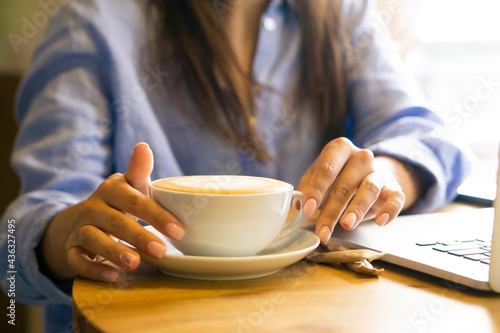 woman hands holding a white cup of capuccino coffee standing on the table in cafe.