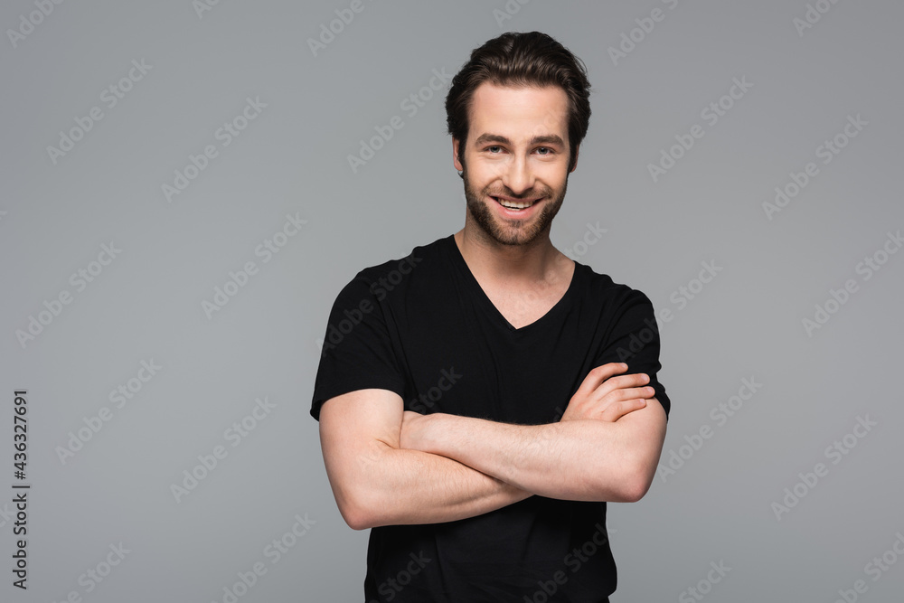smiling man in black t-shirt standing with crossed arms isolated on grey. - obrazy, fototapety, plakaty 