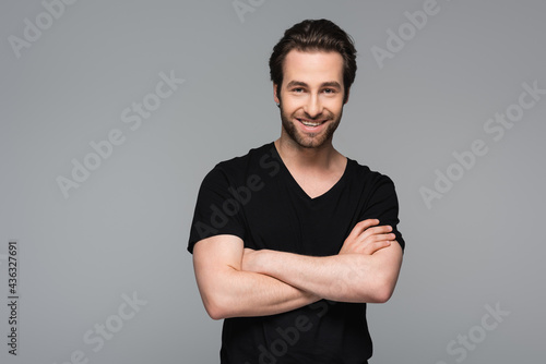 smiling man in black t-shirt standing with crossed arms isolated on grey.