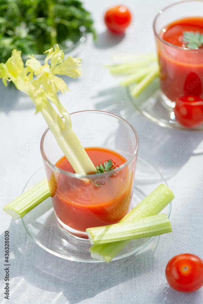 Two glasses with fresh tomato juice, celery, parsley and ripe tomatoes on light wood background Two glasses with fresh tomato juice, celery, parsley and ripe tomatoes on light wood background
