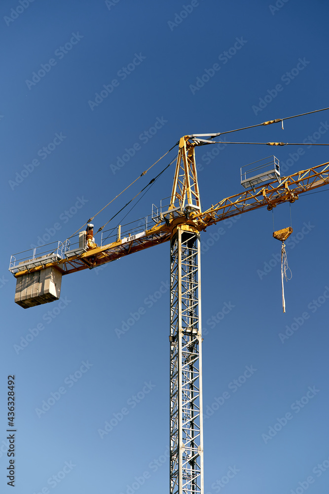 Tall yellow tower crane against the blue sky. Close-up