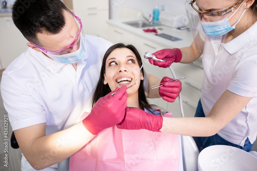 Young smiling woman in a dental chair. Two dentists check the teeth and do their hygiene. Healthcare, medicine