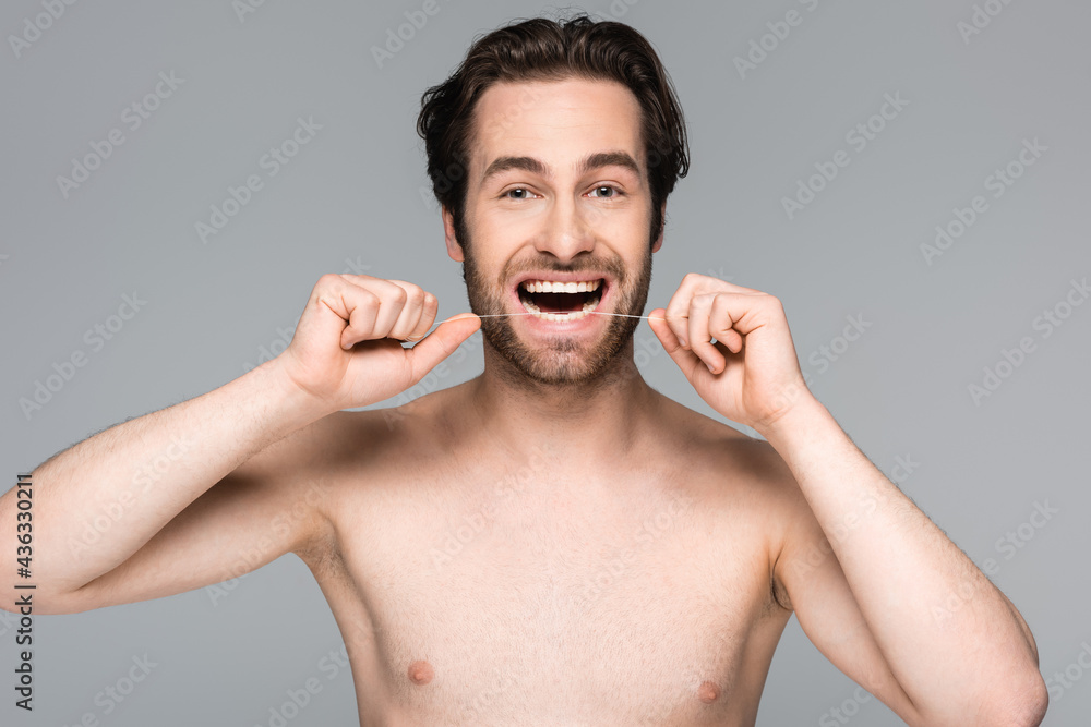 Fototapeta premium happy and shirtless man flossing teeth isolated on grey.