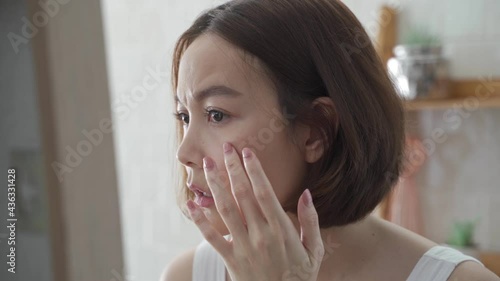 attractive beautiful short hair asian woman worry looking into mirror for face skin care condition. Frustrated Young female Examining Her Face While Looking At The Mirror in bathroom. annoy facial age