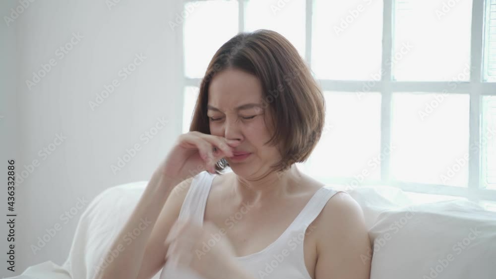 asian woman in white allergy and sneezing on sofa in living room day time. Irritated nose sneeze. authentic lifestyle at home. asian woman in white allergy and sneezing on sofa in living room day time. Irritated nose sneeze. authentic lifestyle at home.