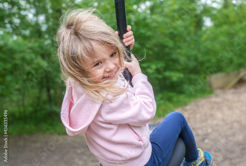 Little girl rides on Flying Fox play equipment. Child girl is smiling in a children's playground. Summertime.