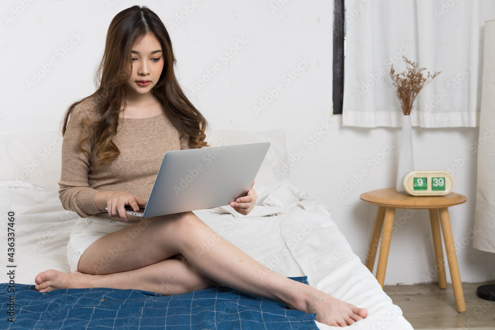 Fototapeta premium An Asian woman working on her bed in her home. She is typing on her notebook.