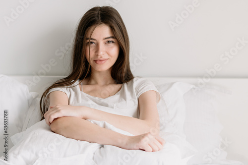 Young woman lying on bed in white bedroom