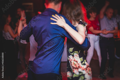 Couples dancing traditional latin argentinian dance milonga in the ballroom, tango salsa bachata kizomba lesson in the red, purple and violet lights, dance festival